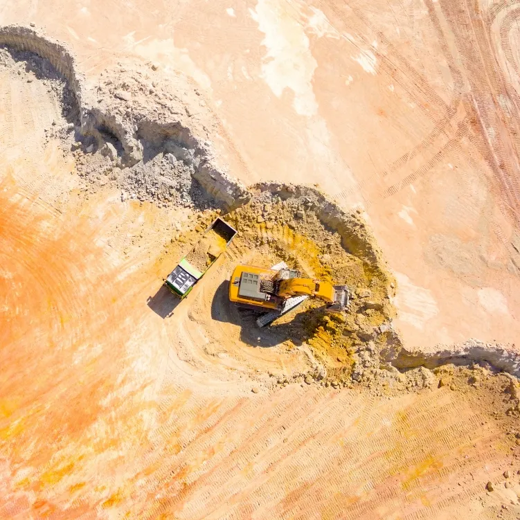 Aerial view of heavy machinery working in a large, open-pit mining area, moving earth and rocks.