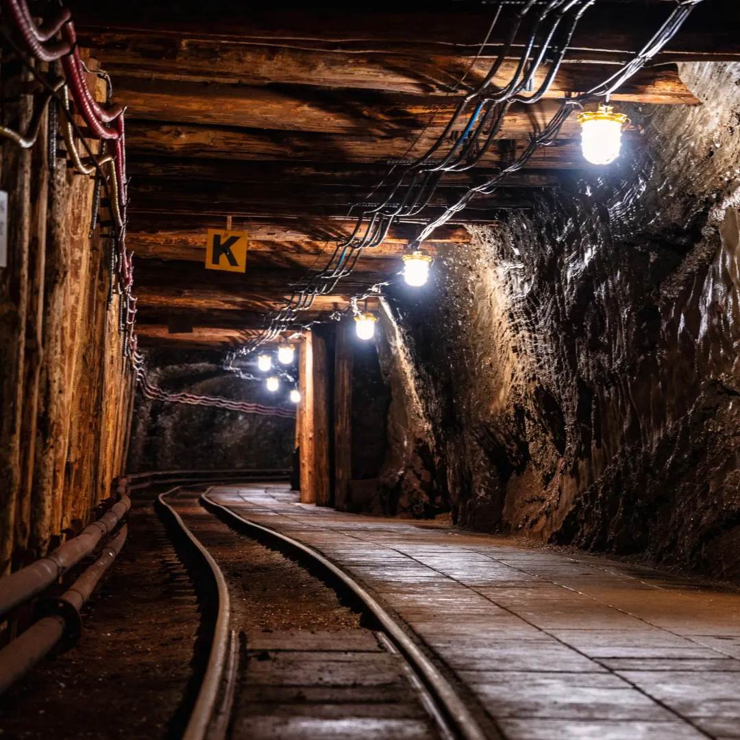 An illuminated underground mining tunnel with wooden supports and a track running through it.