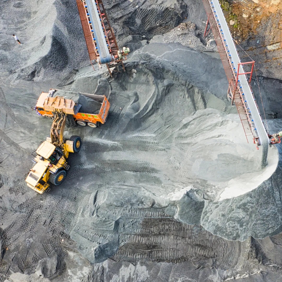 Mining operation with conveyor belts and machinery transporting raw material in a large, open mining area.
