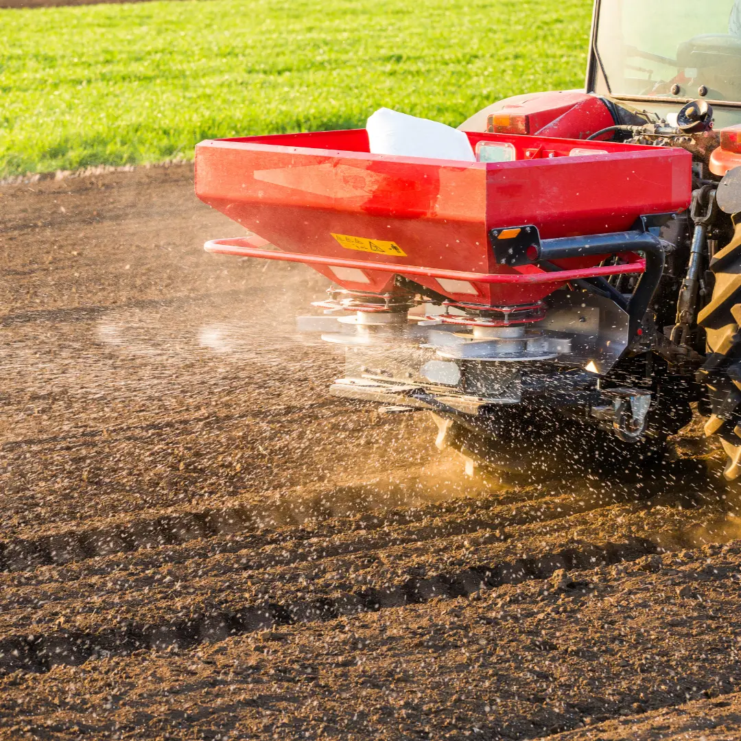 A tractor with a sprayer attachment dispersing fertilizer over a field.