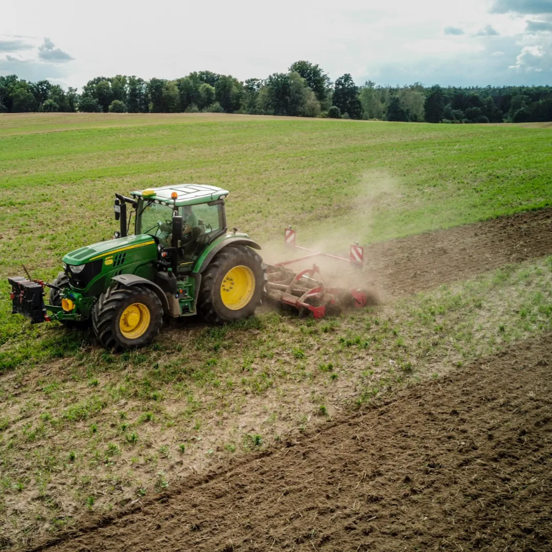 A tractor spreading fertilizer or soil treatment in an open field with a forested background.