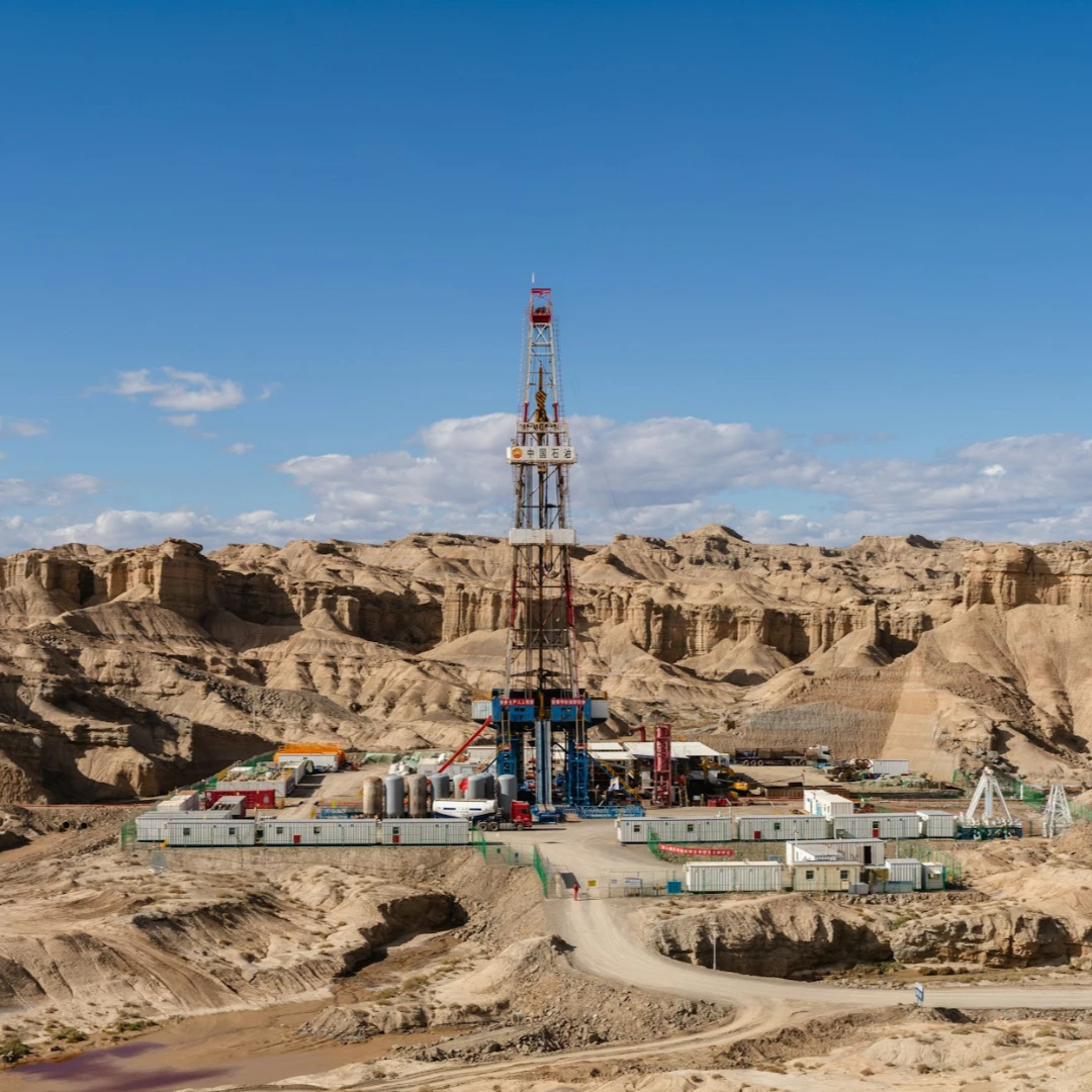 A drilling rig set against a desert landscape with rugged, rocky formations.