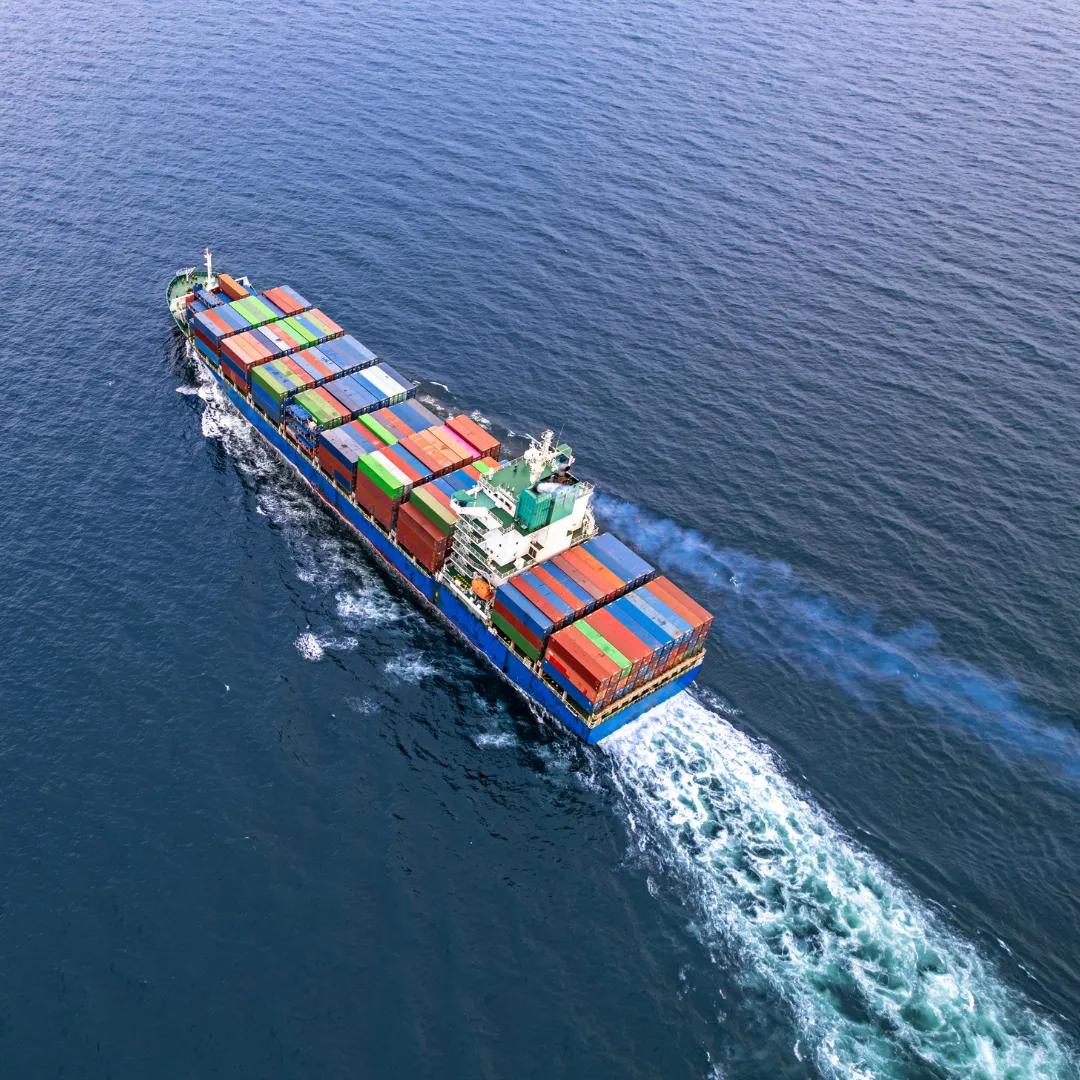 A large cargo ship carrying colorful shipping containers, traveling through blue ocean waters.