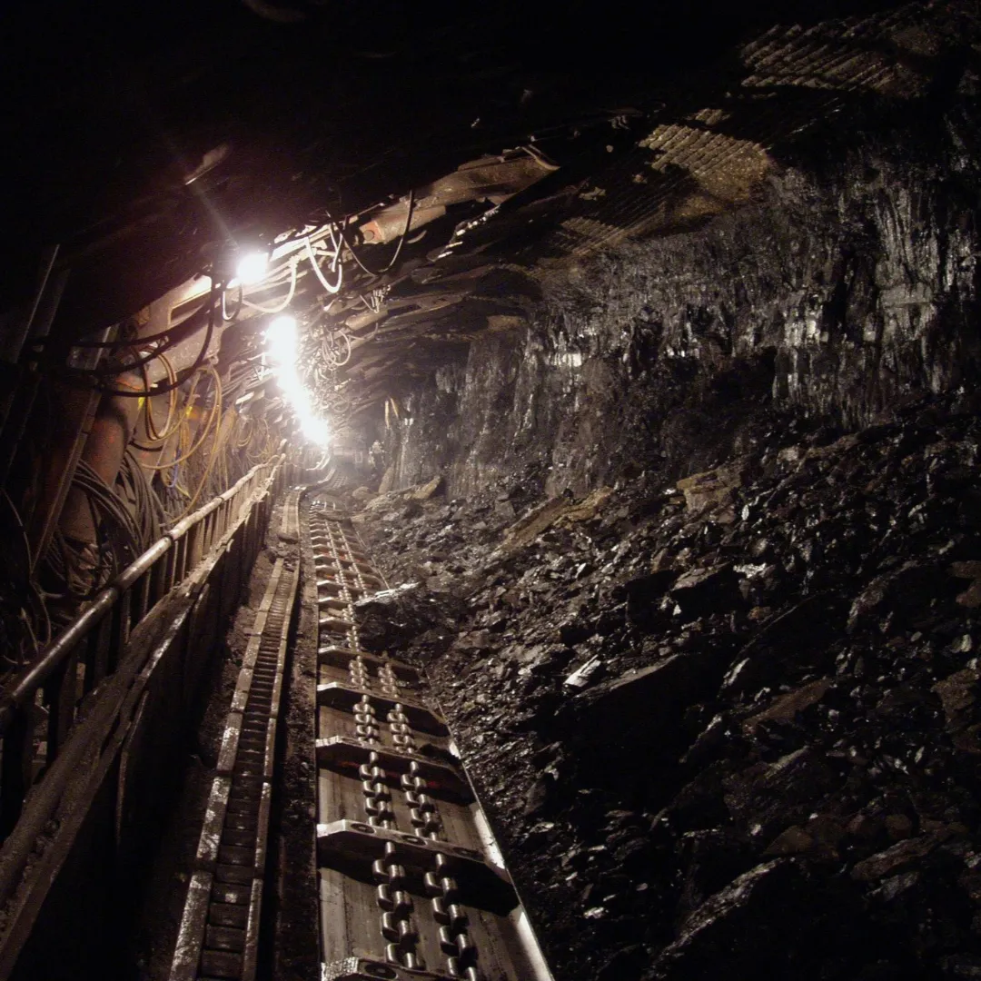 Inside a dimly lit underground mine, showing tracks and mining equipment along a tunnel.