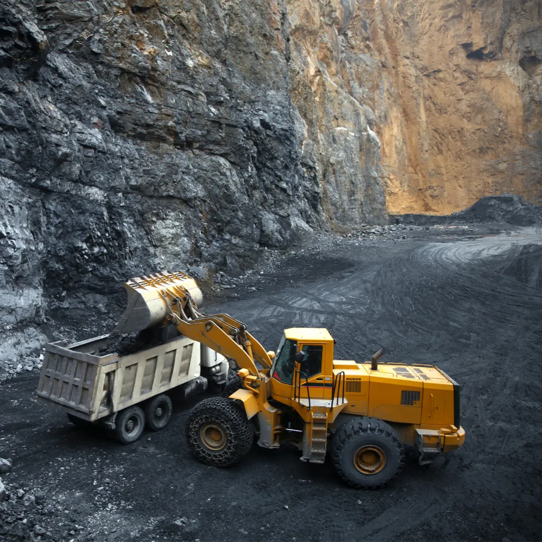 A large yellow truck operating in an open-pit mine, surrounded by rocky terrain.