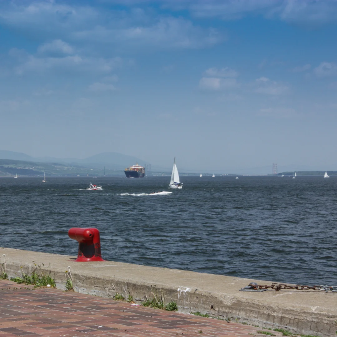 A body of water with sailboats and a buoy, likely an ocean or large lake under clear skies.