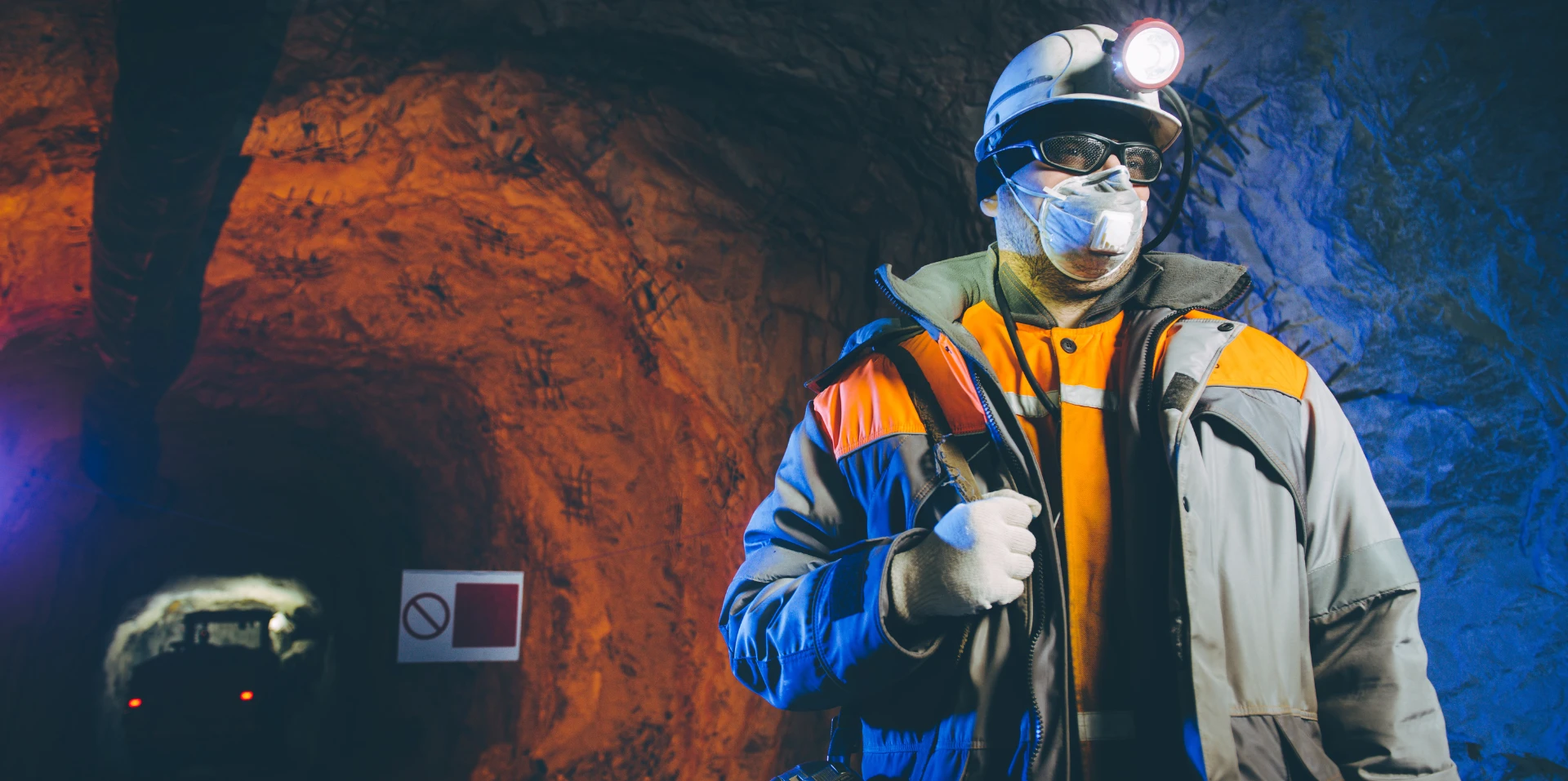A miner wearing protective gear, including a helmet, mask, and reflective jacket.