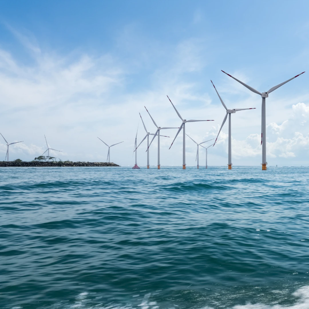 Offshore wind farm with multiple wind turbines standing in the ocean under a blue sky.